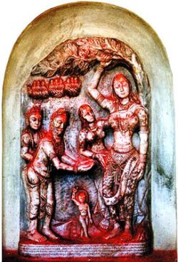 This bas relief depicts Maya Devi with her right hand holding on to a sal tree with a newborn child standing upright on a lotus petal, shedding an oval halo, around his head. This nativity scene of th