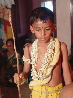 A Tulu Madhwa Brahmin boy during his upanayana ritual. The thin, yellowed, Yajnopavita thread runs from left shoulder to waist. Note the munja grass girdle around the waist. The peepal tree twig in hi